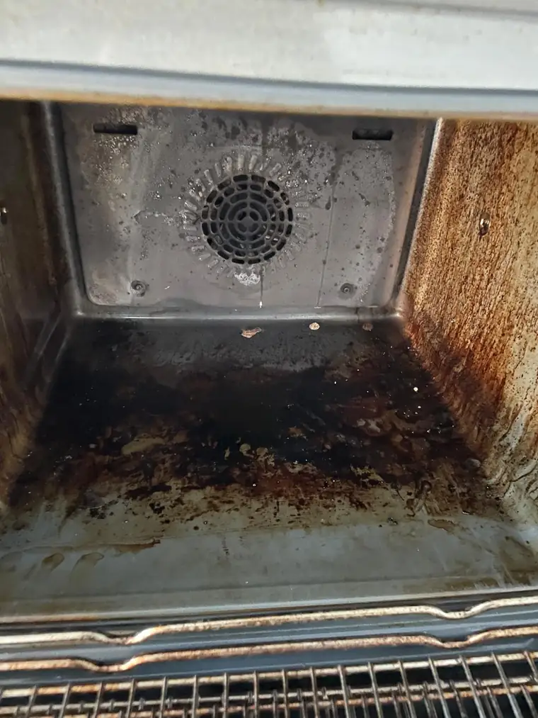 An oven interior before work, with burnt-on grime across the base and rear panel